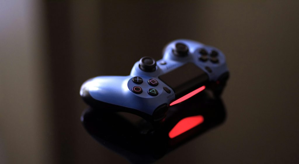 Close-up of a blue PlayStation controller on a glossy black surface with red lighting.